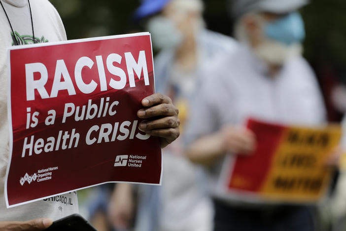 A person holds a sign that says. "Racism is a public health crisis."