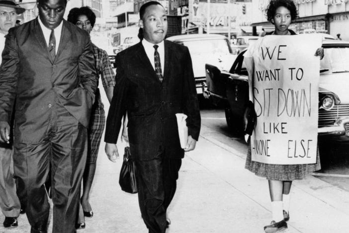 In this Oct. 19, 1960 file photo, Dr. Martin Luther King Jr. under arrest by Atlanta Police Captain R.E. Little, left rear, passes through a picket line outside Rich's Department Store, in atlanta.
