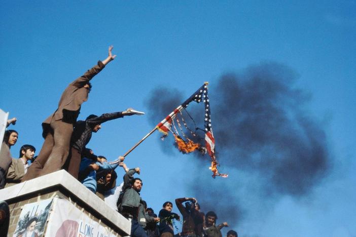 Men stand on a roof with a burning American flag.