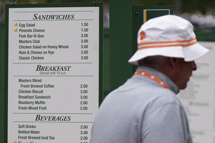 A patron walks past a sign displaying the prices of food items during a practice round in preparation for the Masters golf tournament at Augusta National Golf Club Tuesday, April 9, 2024, in Augusta, Ga. 