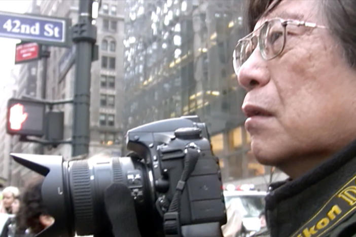 Photographer Corky Lee holding a camera on 42nd Street in Manhattan.