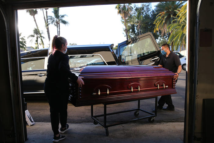 Embalmer and funeral director Kristy Oliver (left) and funeral attendant Sam Deras load the casket of a person who died after contracting COVID-19 into a hearse in El Cajon, Calif. People who work in hospitals and in funeral homes are witnesses to the loss than many Americans can avoid.