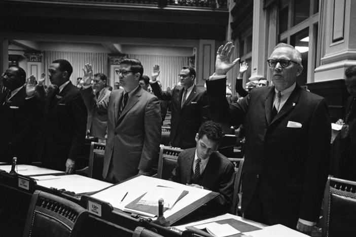 Rep.-elect Julian Bond, center, who was refused a seat in the Georgia House, looks through his desk as two of his Fulton County colleagues, Reps. Jack Etheridge, left, and Charlie Brown raise their hands for the oath of office in Atlanta, Jan. 10, 1966.