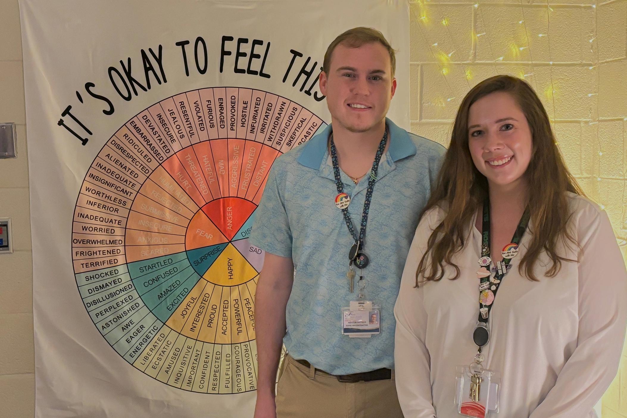 Keaton Warner and Jillian Canada stand in front of a poster with a wheel of feelings at Roswell High School.