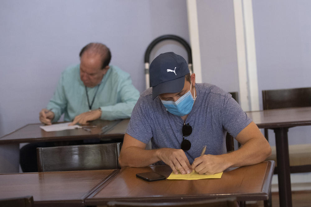 A voter wearing a mask writes on a piece of paper.