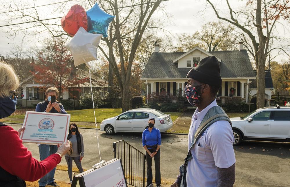 Macon postal carrier Tony King, right, as Susan Cable, left, reads a declaration of “Tony King Day” for the Ingleside neighborhood Monday. King has carried mail for 20 years in the neighborhood and has been working over time during this pandemic holiday season.