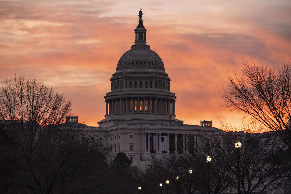 The U.S. Capitol stands silhouetted by the rising sun in the dawn.