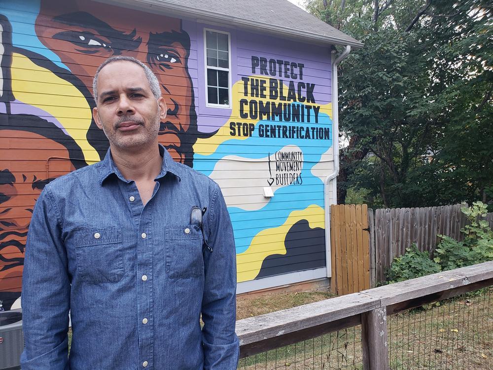 Kamau Franklin stands in front of his mural that says protect the Black community, stop gentrification.
