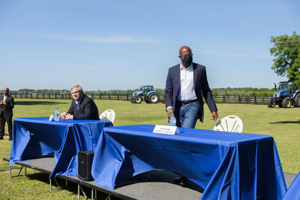 Senator Raphael Warnock, right, takes his seat next to USDA Secretary Tom Vilsack at an event held to explain new USDA debt aid to Black farmers at Fort Valley State University. 