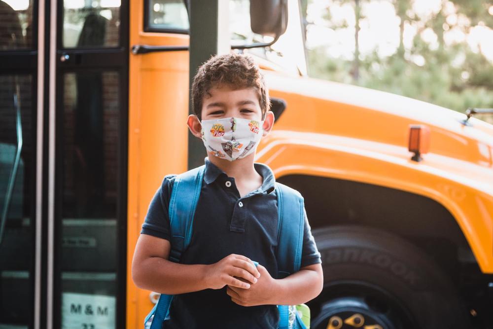 Student standing in front of bus wearing mask.