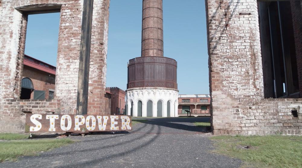 A large wooden sign reads “Stopover” in bold capital letters. It is situated on the ground, outside the Georgia State Railroad Museum in Savannah.