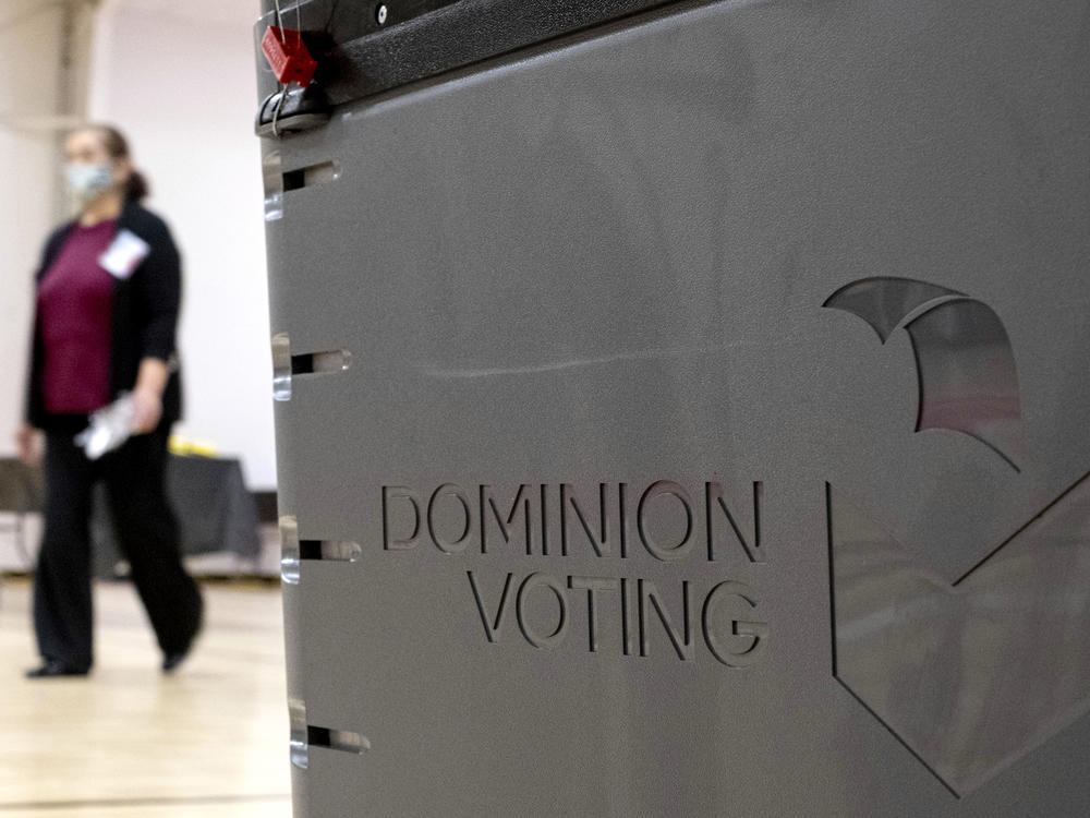 A worker passes a Dominion Voting ballot scanner while setting up a polling location at an elementary school in Gwinnett County, Ga., outside of Atlanta on Jan. 4, 2021. Newsmax has apologized to an employee of Dominion Voting Systems for airing false allegations that he manipulating voting machines or tallies on Election Day to the detriment of former President Donald Trump. Eric Coomer, security director for Dominion, subsequently dropped the conservative news network from a defamation lawsuit. (AP Photo/