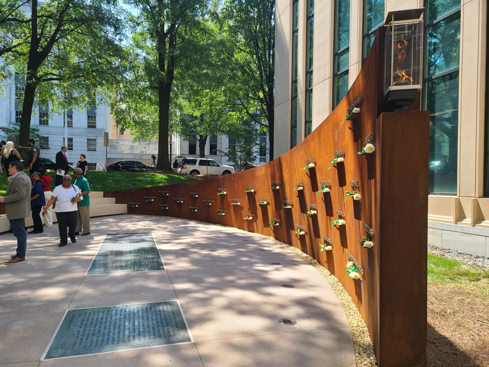 The memorial features a 55-foot steel wall with the names of the 30 victims in white with roses placed in front of them, mostly children, killed between 1979 and 1981 as well as a burning flame.