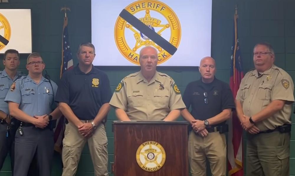 Crisp County Sheriff Billy Hancock is shown behind a podium with law enforcement members standing by his side.