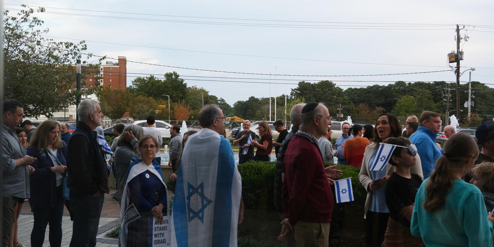 A group of people, some carrying Israeli flags, is shown standing outside.
