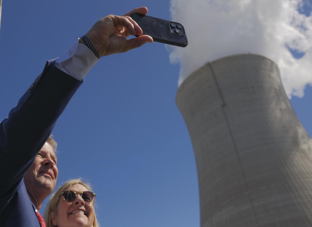Governor Brian Kemp and Georgia First Lady Marty Kemp are shown taking a selfie in front of a nuclear cooling tower.