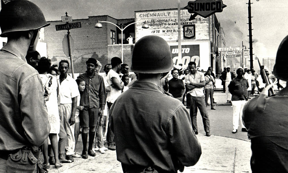 A black and white image of white troops pointing rifles at black citizens.