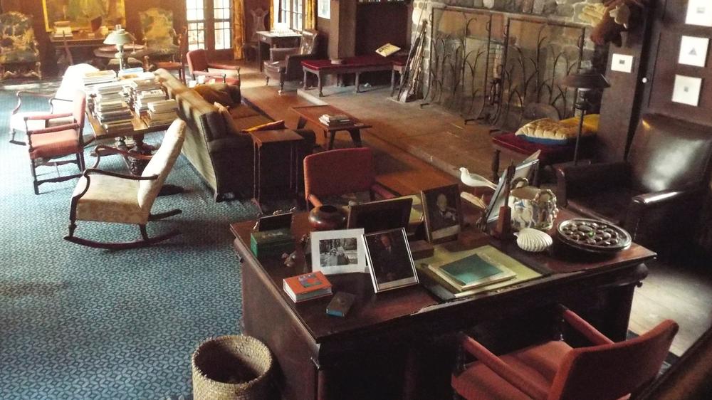 The large main room of the Torrey-West Home is shown, with antique furniture pieces and a desk with several photos on it.
