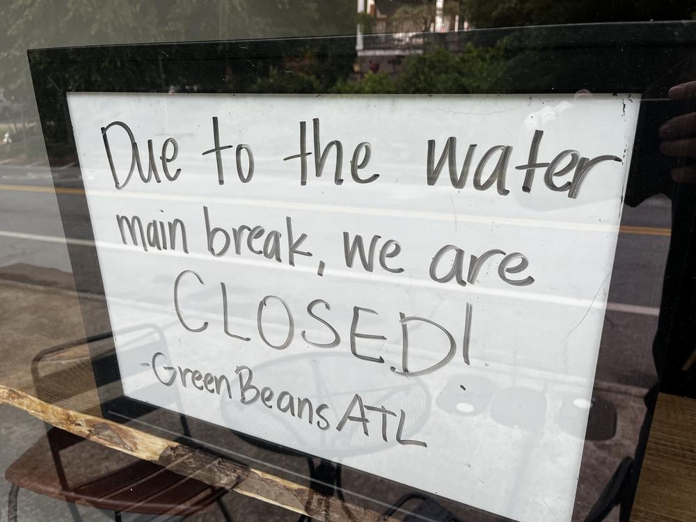 A sign, seen through a window, says "Due to the water main break, we are CLOSED! Green Beans ATL."