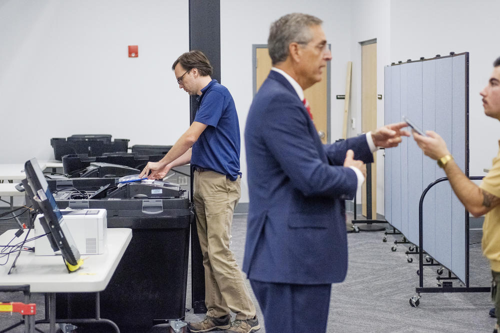 Georgia secretary of state office technician Chris Bellew (left) runs a test on Bibb County elections systems while Secretary of State Brad Raffensperger (right) talks to a reporter Tuesday, July 30, 2024.
