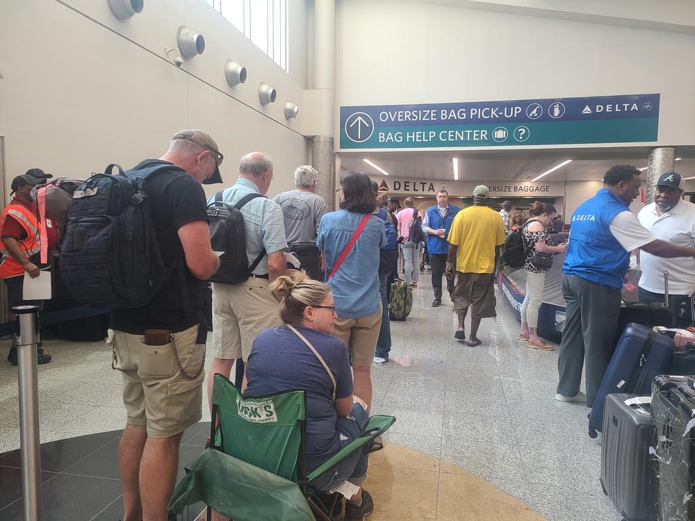 Delta customers wait in line to file a claim for lost baggage and a woman is seated in a green lawnchair