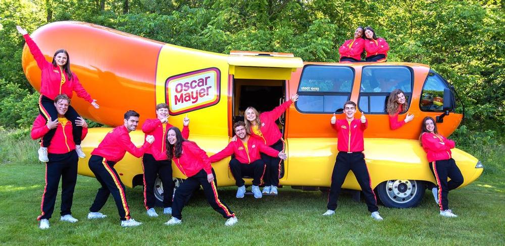 Out of more than 7,000 applicants for the 2024-25 season, Oscar Mayer selected these 12 Wienermobile drivers, including Columbus native Sarah Oney (the person on the right in the “bun roof”). They are posing in Madison, Wisconsin, where the drivers trained for two weeks in June 2024. Courtesy of Sarah Oney