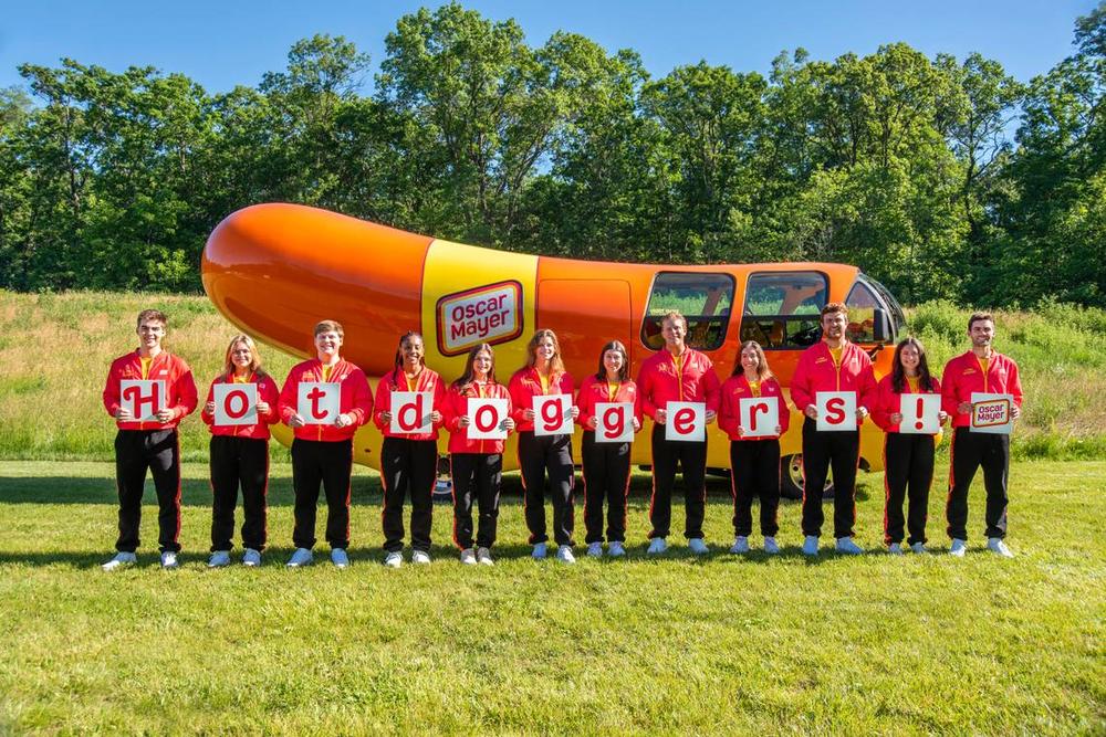 Out of more than 7,000 applicants for the 2024-25 season, Oscar Mayer selected these 12 Wienermobile drivers, including Columbus native Sarah Oney (seventh from left). They are spelling the word “Hotdoggers,” the title for Wienermobile drivers, as they pose in Madison, Wisconsin, where they trained for two weeks in June 2024. Courtesy of Sarah Oney