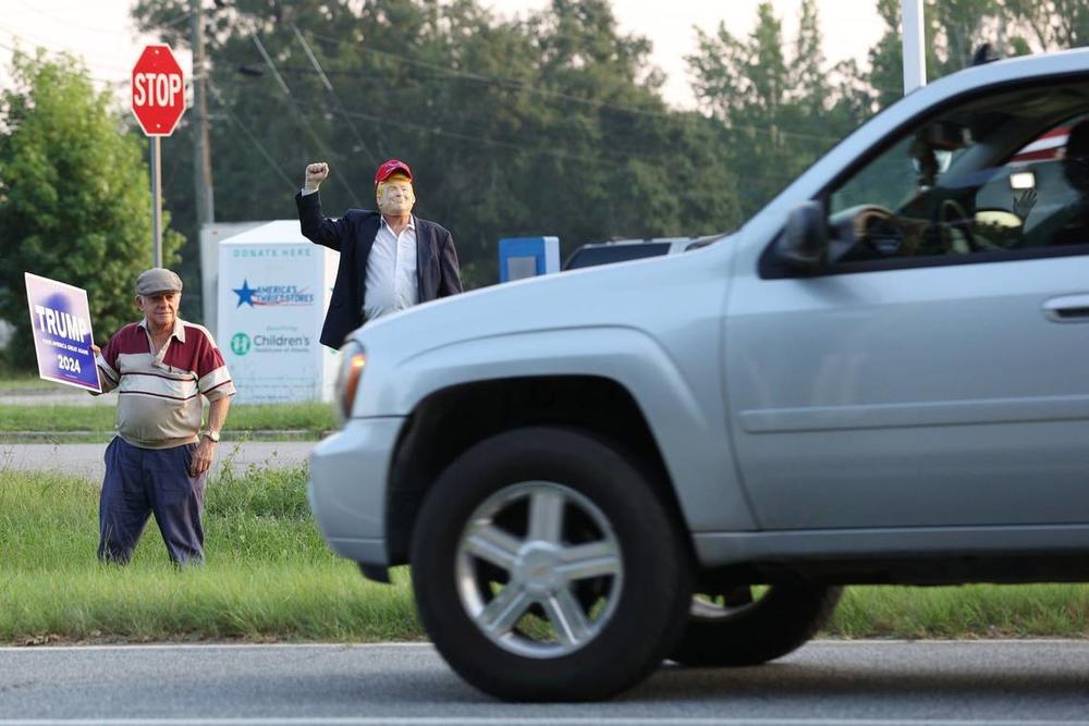 Tom Brown (left) and David Sumrall in a Donald Trump mask react to a honking car on Eisenhower Parkway on Monday, July 15, 2024, in Lizella, Georgia. A half dozen supporters, including members of the Bibb County Republican Party, gathered to show their support for former president Trump two days after an attempted assassination attempt on him in Pennsylvania. Katie Tucker/The Telegraph