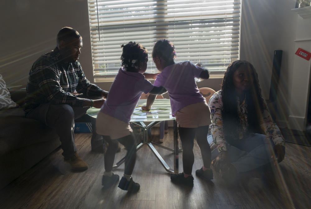 Justice Altidor and her twin sister, Journey, center, play in between their parents at home.