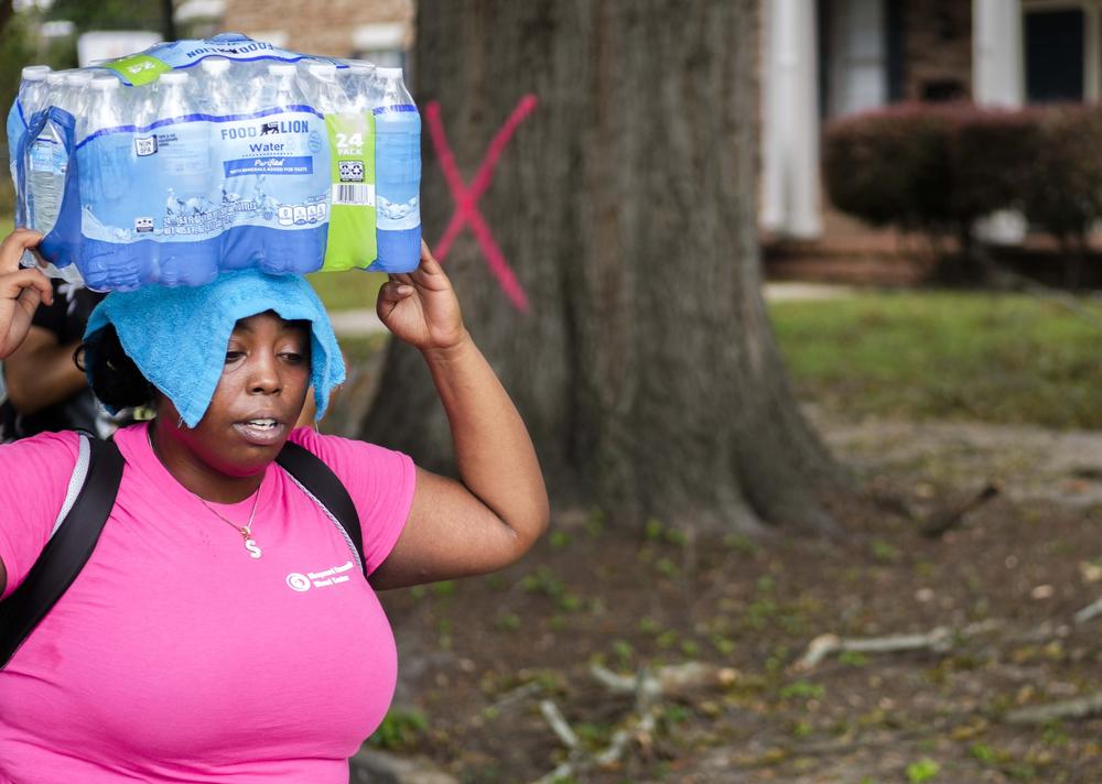 Shaday Collins balances bottled water on her head for a miles long walk back home from one of the Augusta distribution sites.