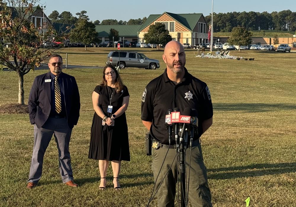 Barrow County Sheriff Jud Smith and two other people are shown standing on the grass lawn in front of Apalachee High School.