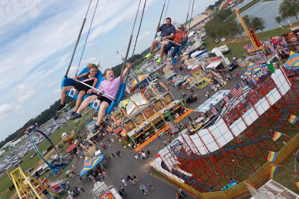 The Hargraves Family rides on the swings at the Georgia National Fair in Perry, Georgia on Saturday, October 5, 2024. Paisley, 9, left, holds hands with Cherise, 7, right, with parents Kohle, left, and Courtney, right, behind them. The family plans to make visiting the fair a yearly tradition as a way to spend time together. Paisley's favorite part about the fair was the rides, specifically the ones that make you dizzy. Cherise's favorite part was the trampoline. (Photo/Adam Walters)