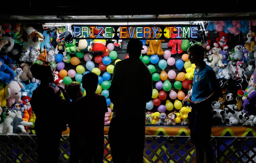 A family stands silhouetted by a fair booth which reads "Prize Every Time" while walking along the midway of the Georgia National Fair in Perry, Georgia, on Saturday, Oct. 5, 2024. Reithoffer Shows, a North American traveling midway founded in 1896, provides the attractions at the Georgia National Fair. (Photo/Felix Scheyer)