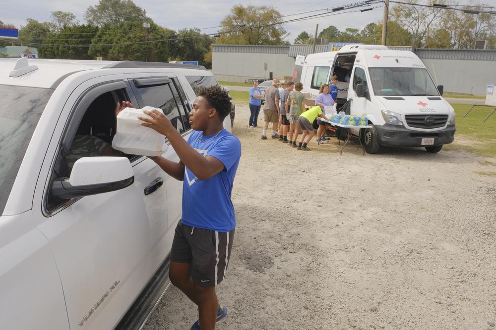 A young man is shown handing a plastic bag of food to a person inside of a car.