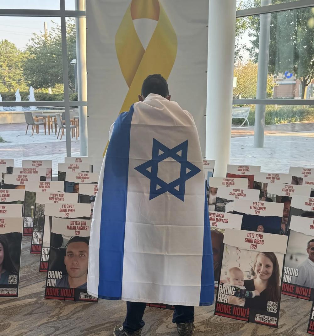 A man draped in an Israeli flag stands before a memorial to hostages still held after the Oct. 7 Hamas attacks in 2023.