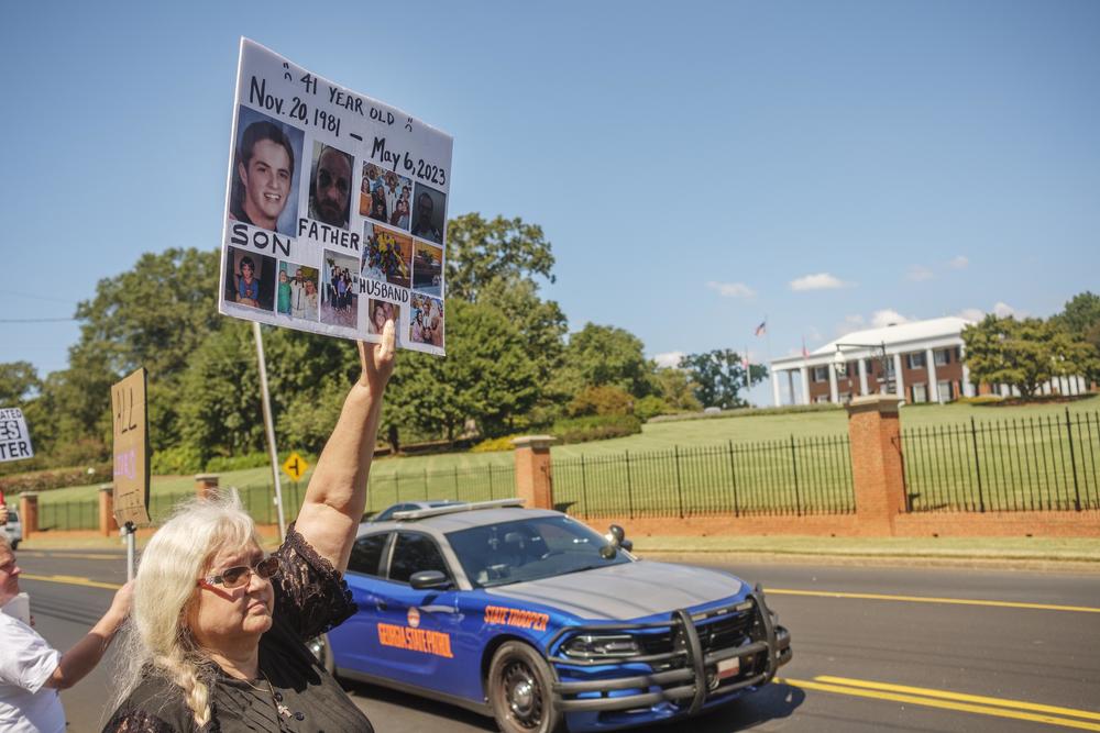 Carrie Proffitt protests in 2023 across from the Georgia Governor's Mansion with photos of her son who took his own life in a Georgia Department of Corrections prison.