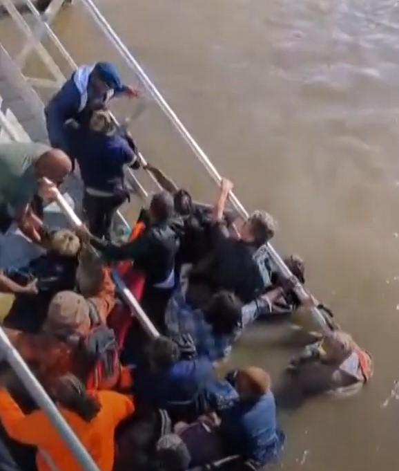 A screenshot from an online video shows about a dozen people struggling in muddy water moments after a dock collapsed.