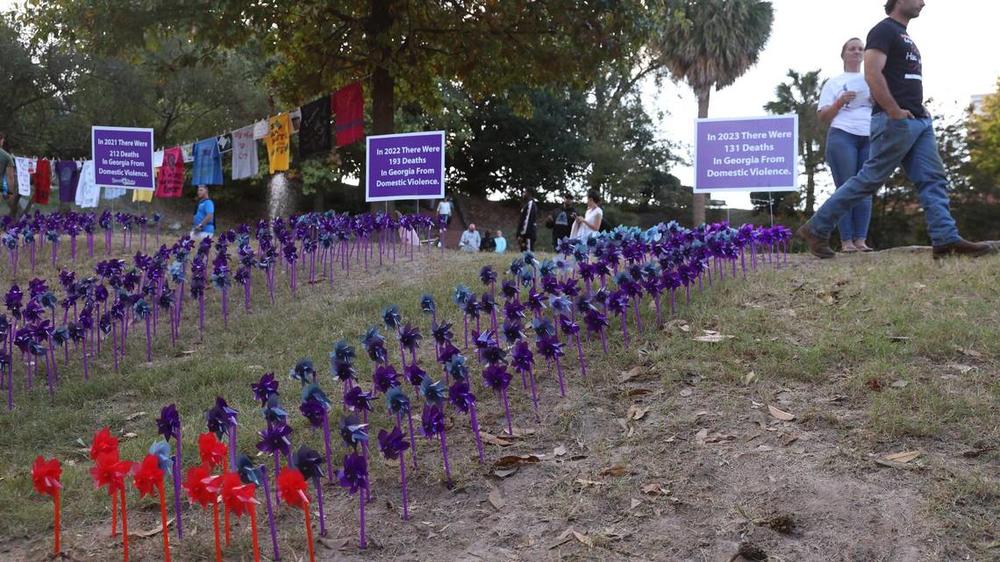 A vigil attendee walks by the pinwheel project as a part of the Domestic Violence Awareness Month candlelight vigil in Washington Square Park on Tuesday, Oct. 29, 2024, in Macon, Georgia. Each pinwheel represents one death from domestic violence in Georgia and the red pinwheels represent deaths in Middle Georgia. Katie Tucker/The Telegraph