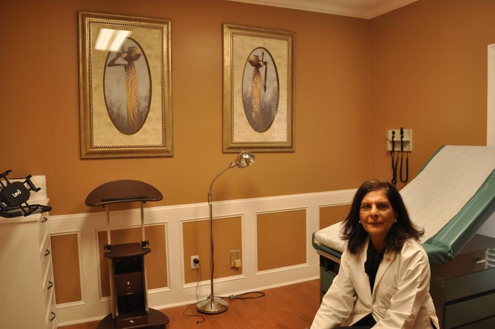 Dr. Gulshan Harjee, co-founder of the Clarkston Community Health Center, sits in front of two paintings in a clinic examination room on Thursday. (Allen Siegler / Healthbeat) 