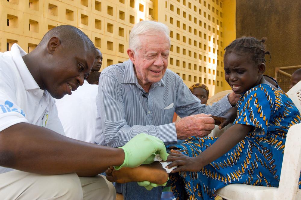 Former U.S. President Jimmy Carter comforts six-year-old Ruhama Issah at Savelugu Hospital on Feb. 8, 2007, as Adams Bawa, a Carter Center technical assistant, dresses her Guinea worm wound.