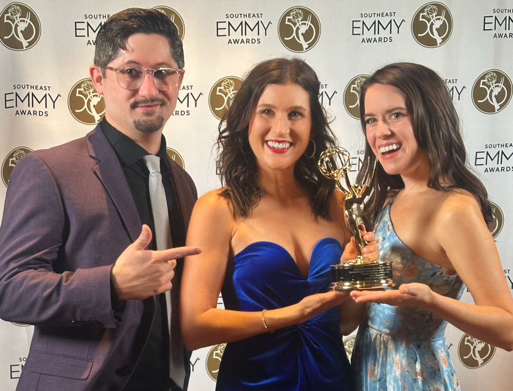 Three people holding an EMMY statue.