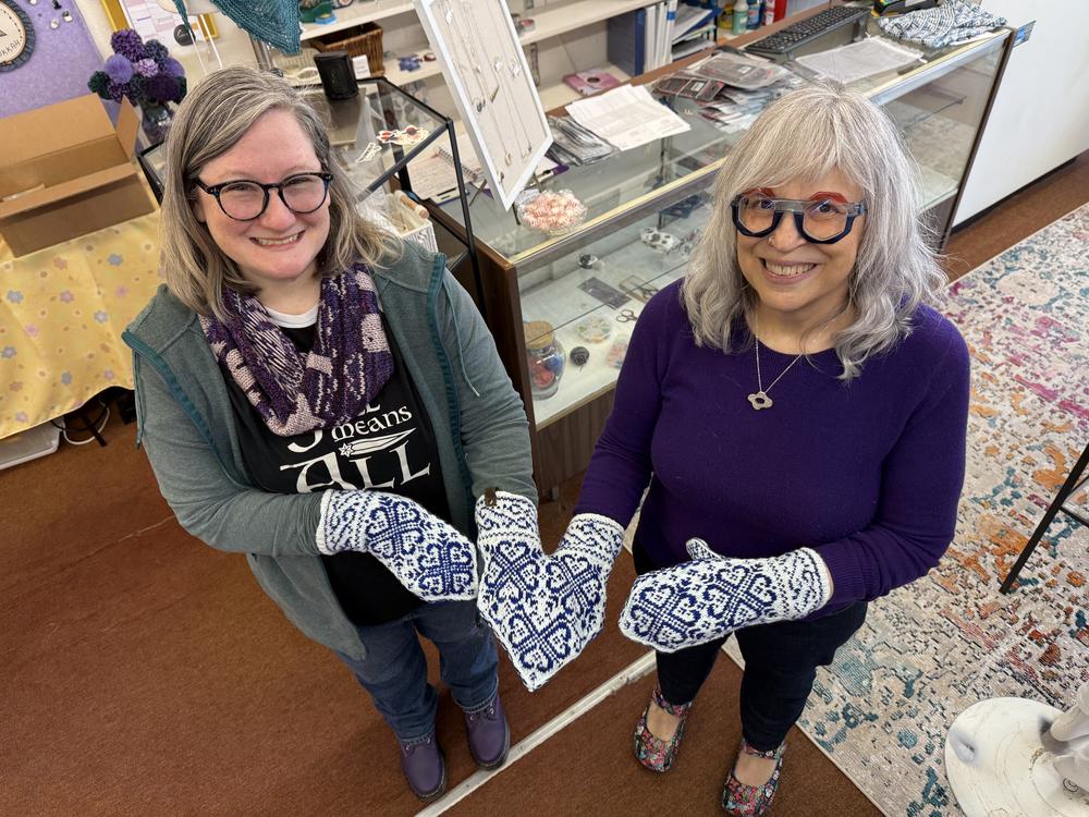 Two women showcasing their knitting work with oven mitts