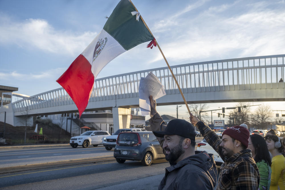 Local resident Saul holds up documents that list a person's constitutional rights if they are approached by federal agents and Juan Bernal (right) waves a Mexican flag during a protest in Gainesville, Ga., on Jan. 29, 2025, against President Trump's immigration policy. "To see all the young people here, lots of them come because their parents cannot," Saul said in Spanish. "This [gathering] demonstrates that there still is some humanity left in the world."