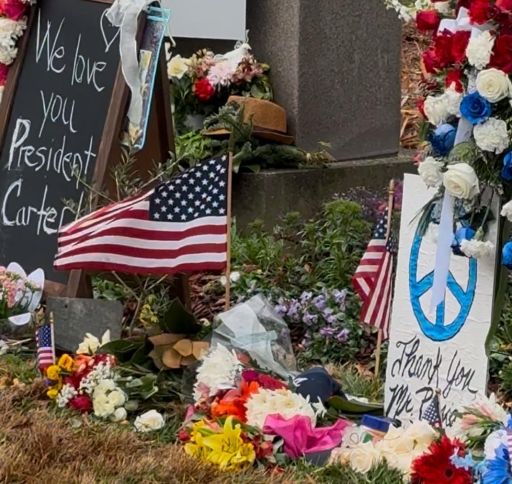 A memorial at the entrance of the Carter Center is covered in flowers, flags and notes from  those who are remembering the life and legacy of former President Jimmy Carter, who died on Dec. 29, 2024.