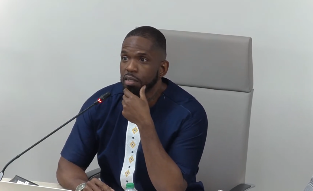 South Fulton Mayor Khalid Kamau wears a blue tunic in front of a microphone at a city council meeting.