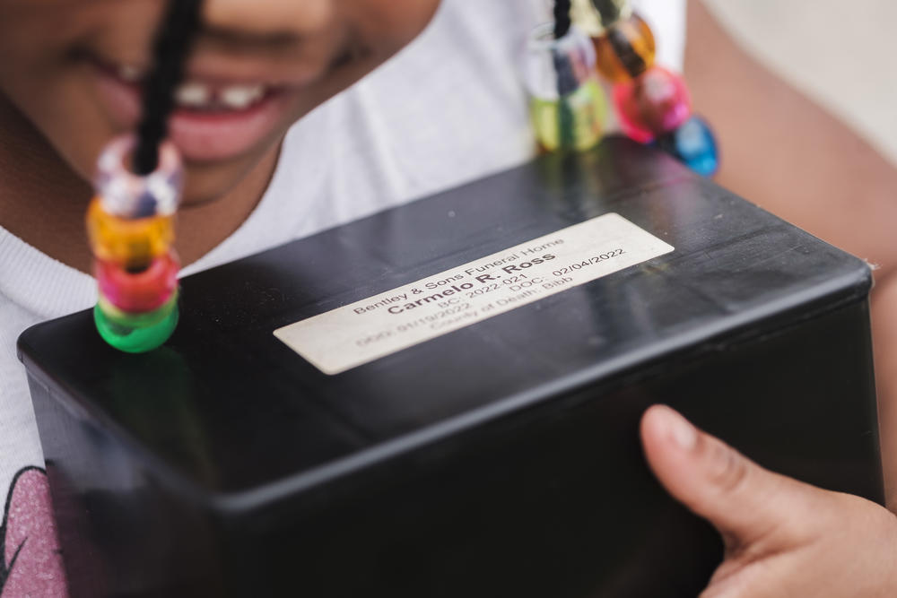 Aylexis Ross, 4, holds the box containing the ashes of her brother Carmelo who was killed in a drive-by shooting in 2022.