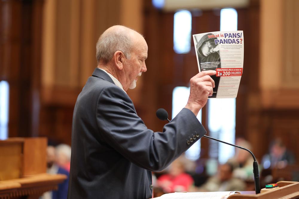 Georgia Rep. Mitchell Scoggins (R-Cartersville) pictured holding information about Pediatric Acute-onset Neuropsychiatric Syndrome (PANS) as he presents House Bill 124 to the House floor on February 25, 2025. Credit: Georgia House of Representatives