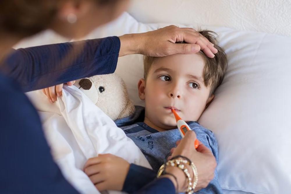 A child lies in bed as an adult holds a thermometer and feels their head