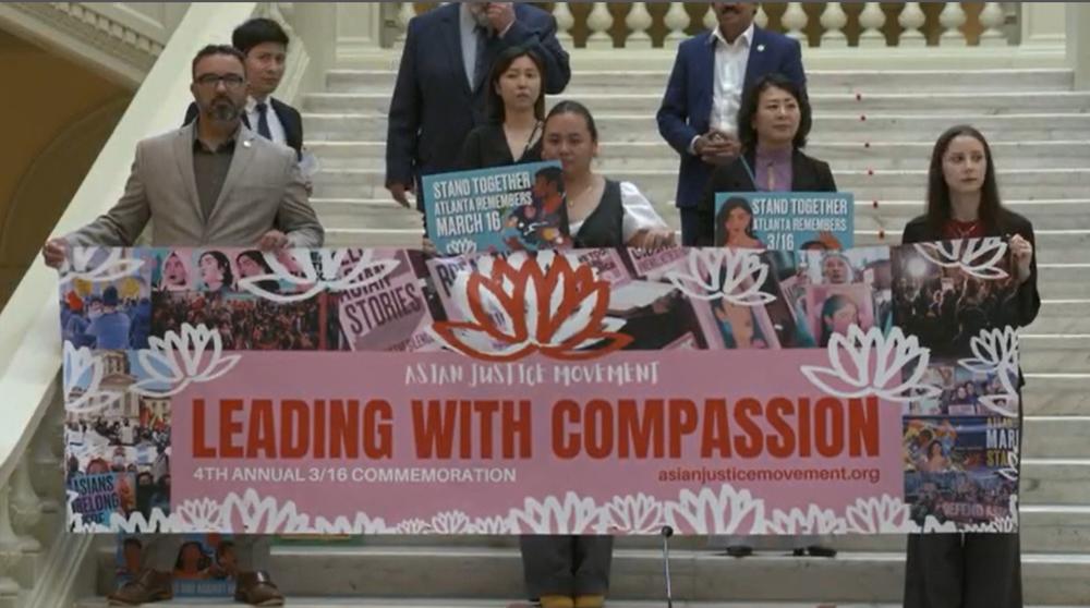 Seven people stand on a wide staircase inside the Georgia Capitol holding a banner that reads "Leading with Compassion."