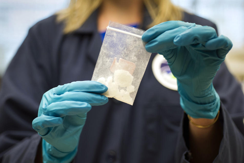 A pair of gloved hands holds a clear, plastic bag with fentanyl.